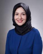A photo of Ayse Yilmaz, wearing a black hijab and a blue blouse, smiling at the camera